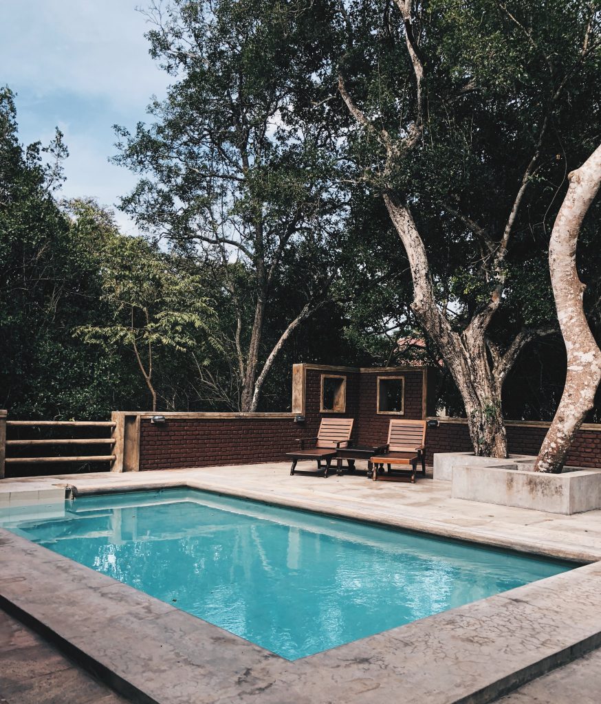 piscine en extérieur avec abord en béton et chaises longues en bois sous les arbres